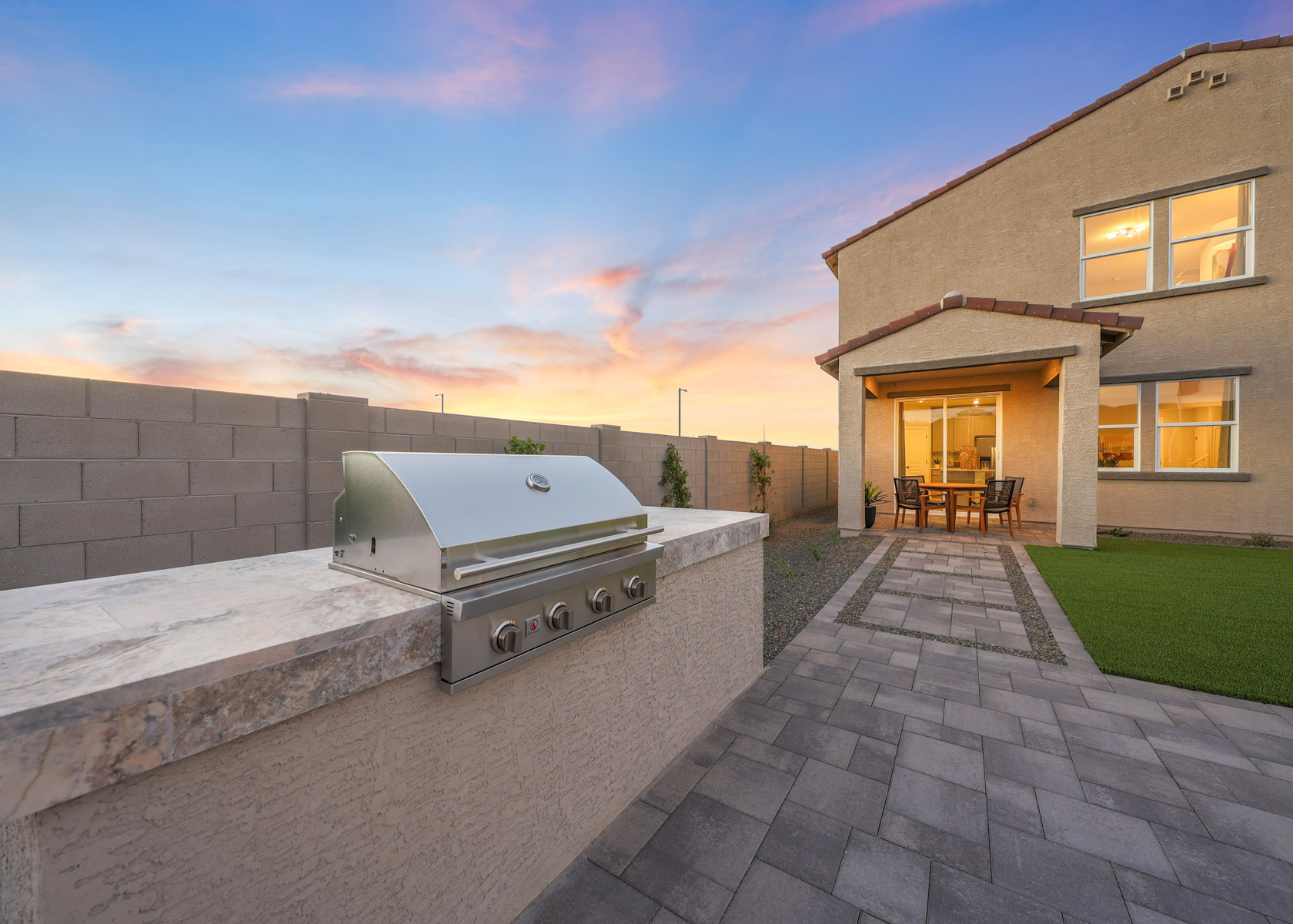 A brick patio with a brick wall and a brick walkway with a house and a blue sky.