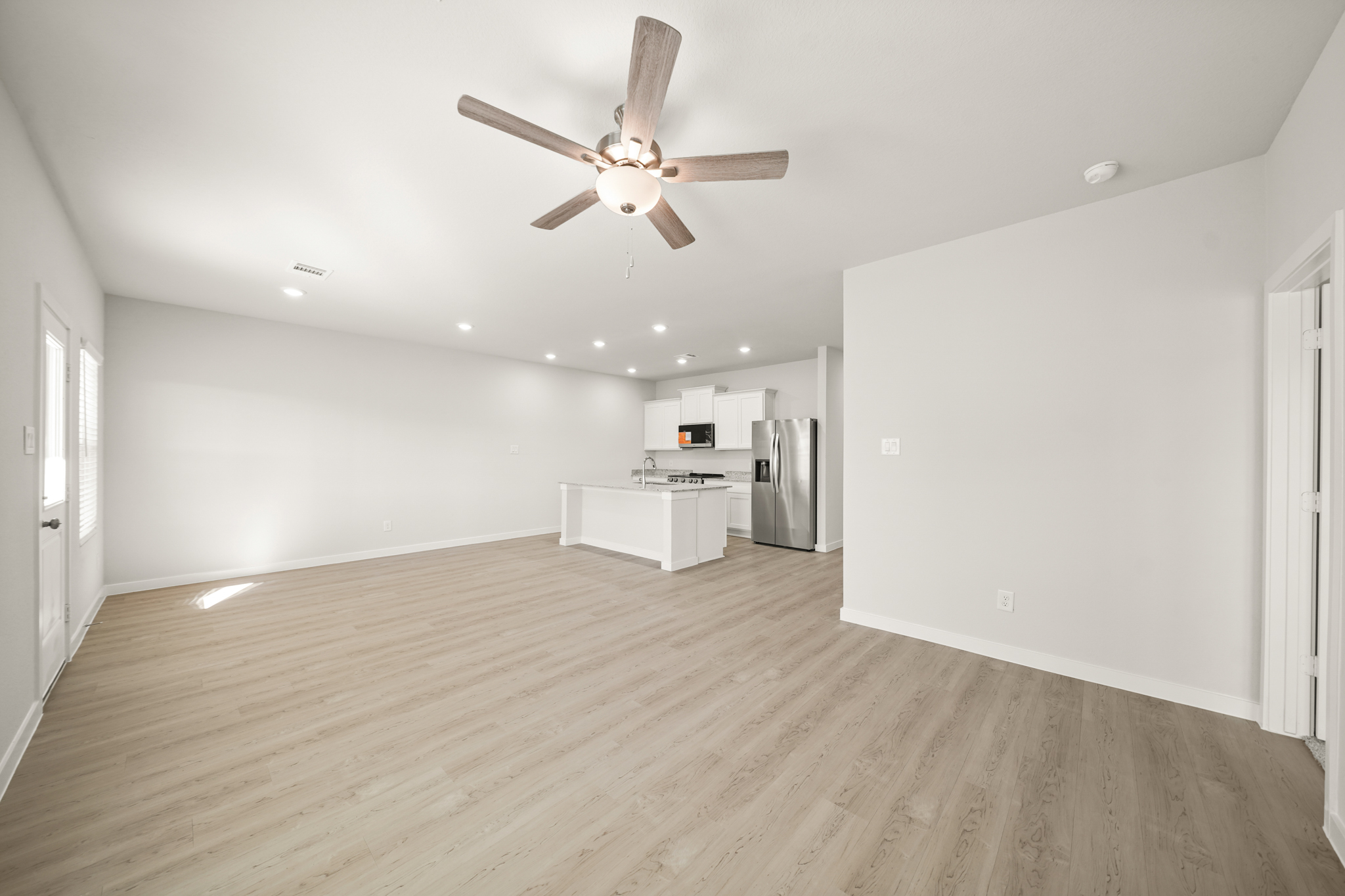 A large empty room with a ceiling fan and a wood floor.